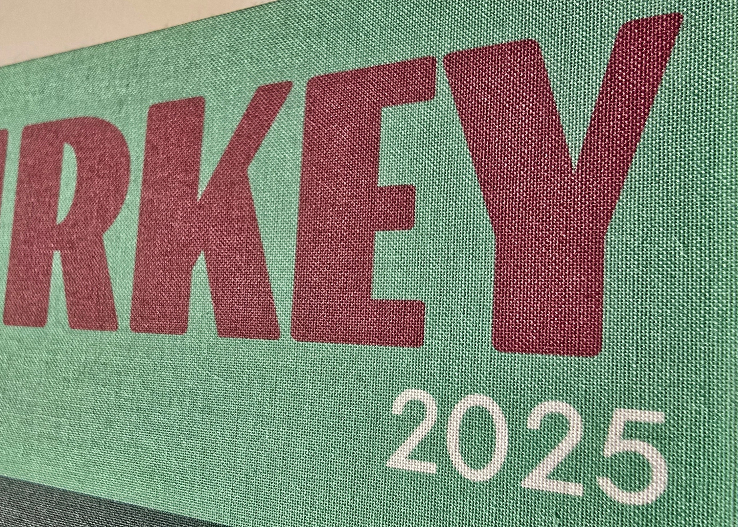 Green sign with 'TURKEY 2025' text on a fabric background
