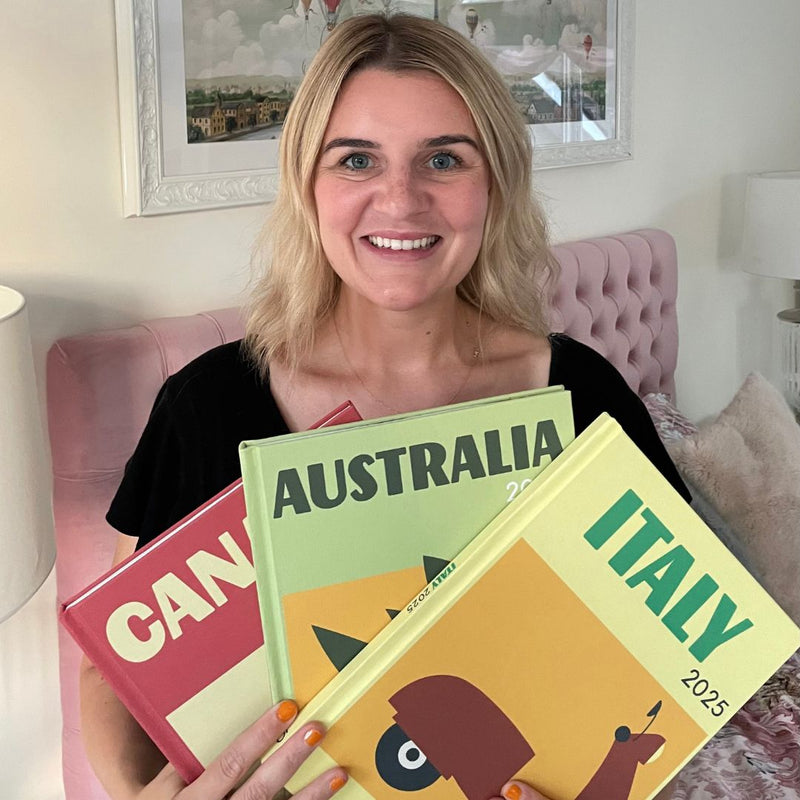 Woman holding books titled 'Canada', 'Australia', and 'Italy' in a room with a pink headboard.