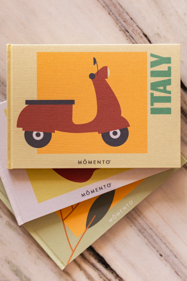 Book titled 'Italy' with a scooter illustration on an orange background, placed on a wooden surface.